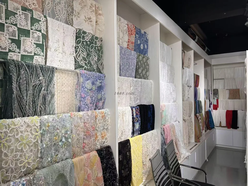 Muestras de encaje y tejidos bordados de color blanco y otros colores, dispuestas en estantes blancos de la exposición de YiTuo.