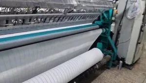 Weißer Stoff in einer Textilmaschine, auf eine untere Rolle aufgewickelt.