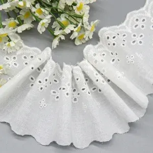 White gathered eyelet trim with flower-shaped holes beside small white flowers. White gathered eyelet trim with flower-shaped holes beside small white flowers.