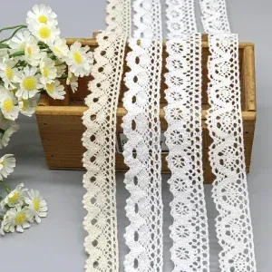 White and ivory scalloped lace trims draped over a wooden box beside small white flowers. White and ivory scalloped lace trims draped over a wooden box beside small white flowers.