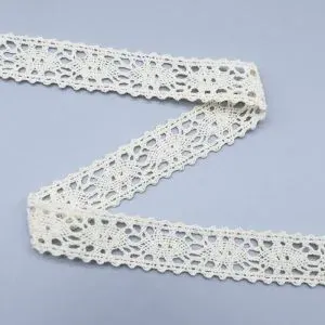 Galon de dentelle ivoire à bords festonnés disposé en zigzag sur une surface grise. Galon de dentelle ivoire à bords festonnés disposé en zigzag sur une surface grise.