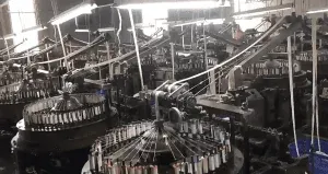 Factory setting showing technicians operating embroidery equipment to produce custom pure cotton eyelet lace with reinforced borders for garments.