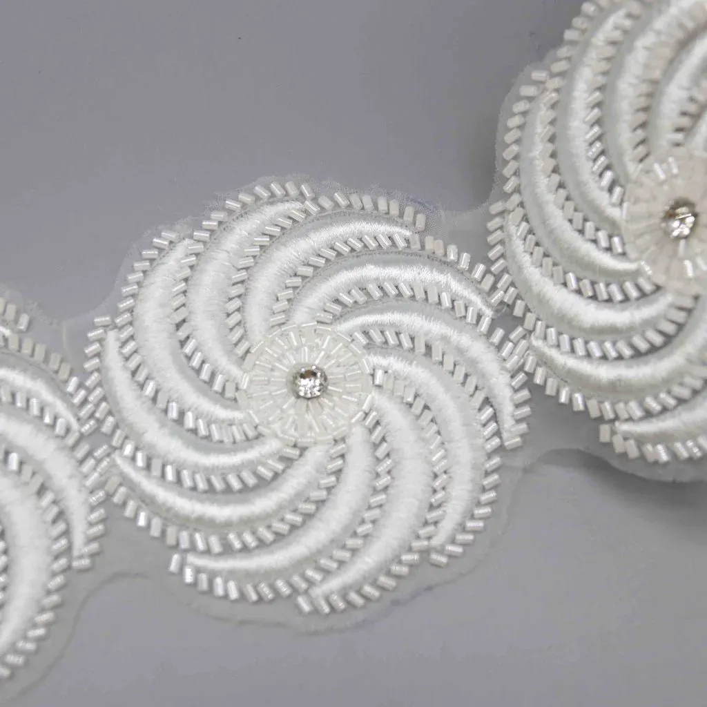 Primer plano de un galón floral blanco en espiral con cuentas tubulares y centros brillantes. Primer plano de un galón floral blanco en espiral con cuentas tubulares y centros brillantes.