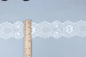 Reinweiße Häkelspitze mit aufwendigen perlenbesetzten Blumenmotiven neben zeitloser Stickspitzenborte für Couture-Kleidungsdetails.