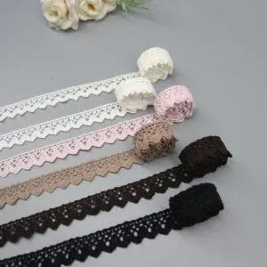 Imagen detallada de una tira de encaje de algodón multicolor de diseño complejo frente a un borde ancho de algodón personalizado y llamativo, ideales para líneas de ropa personalizadas.