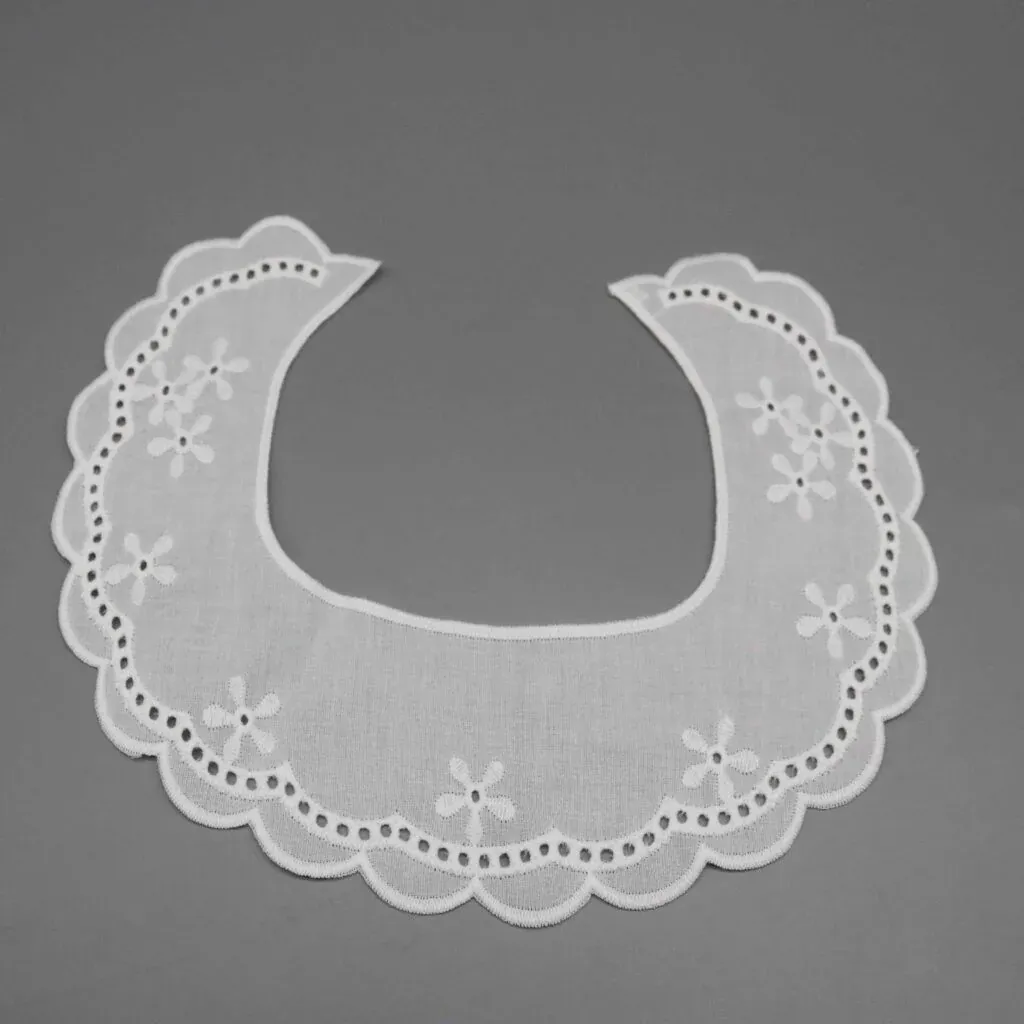 Weißes, gebogenes, kragenförmiges Stickteil mit Blumenmotiven, kleinen Öffnungen und Bogenkante auf grauem Hintergrund. Weißes, gebogenes, kragenförmiges Stickteil mit Blumenmotiven, kleinen Öffnungen und Bogenkante auf grauem Hintergrund.