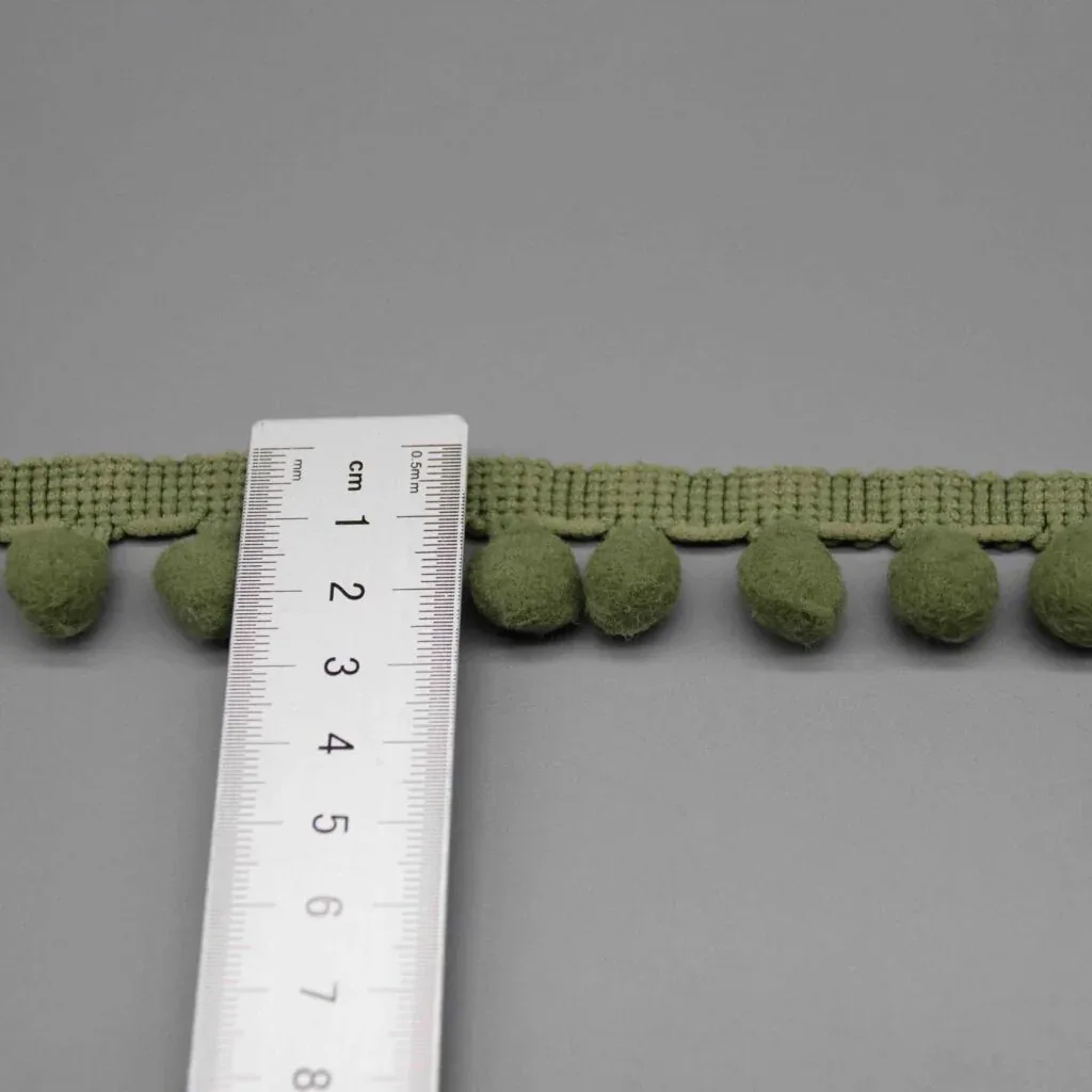 Regla colocada verticalmente sobre la tira de pompones para mostrar su anchura exacta de 2cm Regla colocada verticalmente sobre la tira de pompones para mostrar su anchura exacta de 2cm