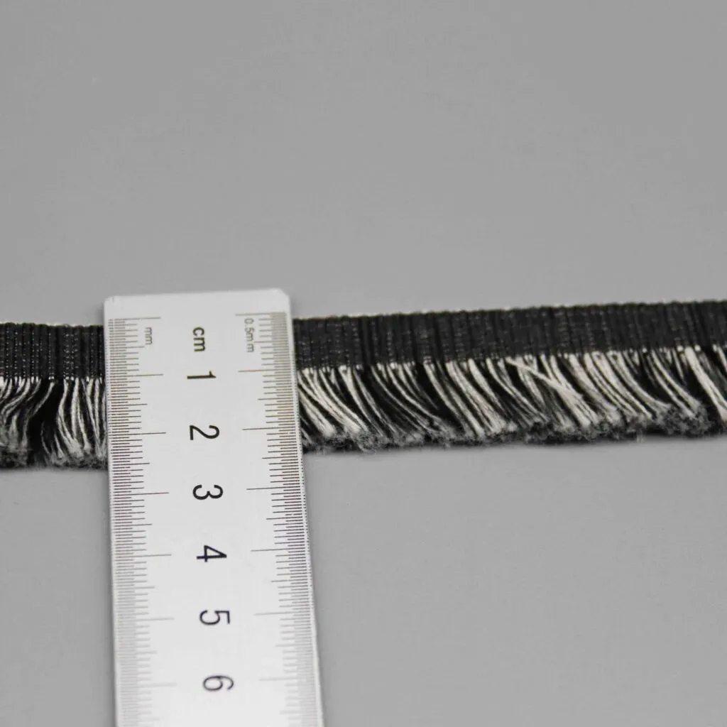 Regla colocada verticalmente sobre los flecos para mostrar su anchura exacta de 2.5cm