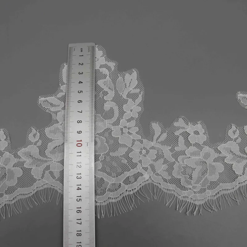 A vertical ruler against a white floral lace peak and the fringed lower edge.