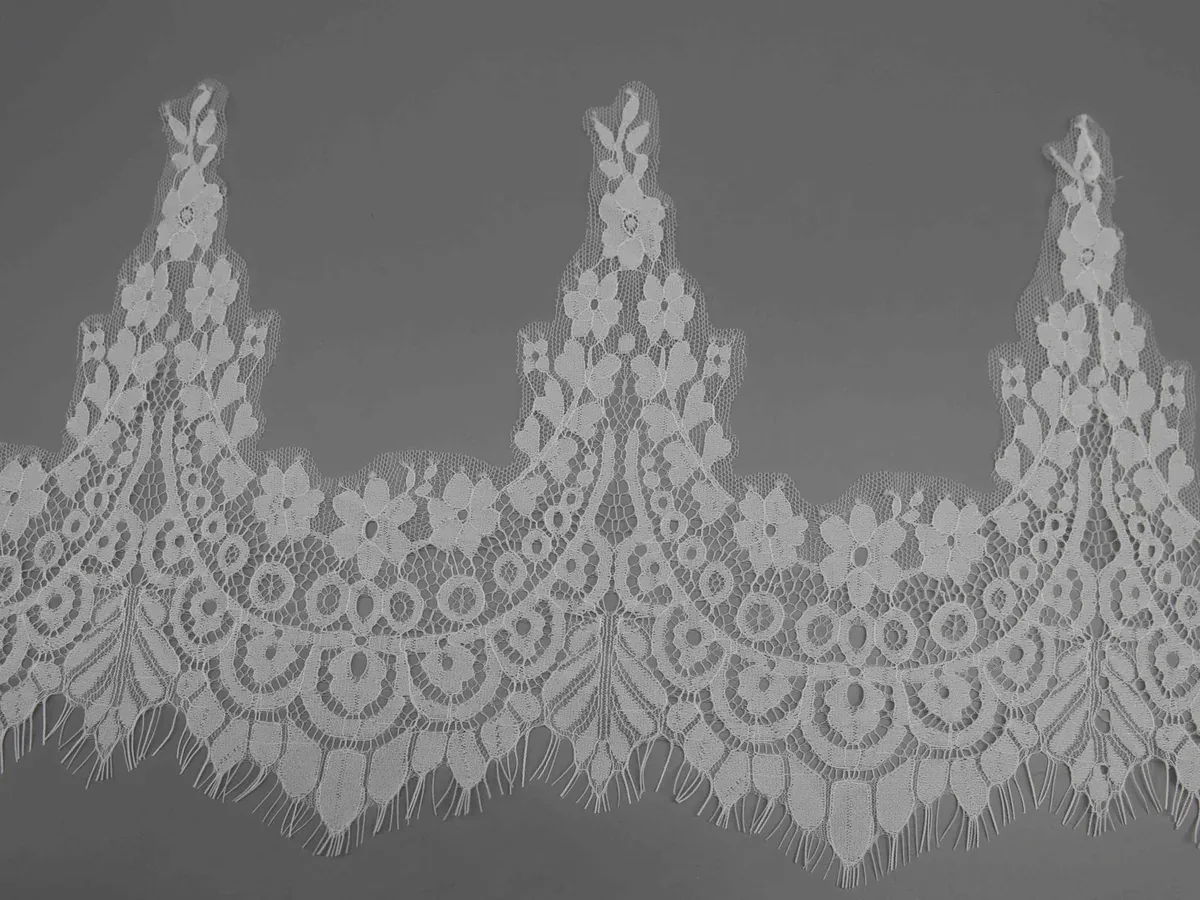 A flat length of white lace showing the repeated deep curves between tall floral peaks.