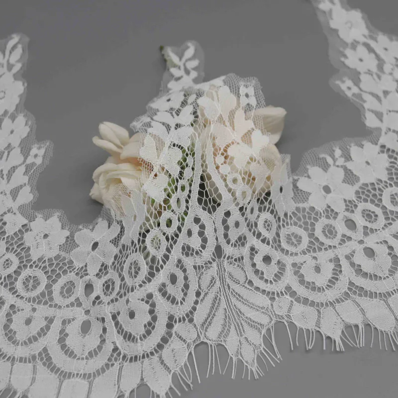 White lace draped over a rose, with open looped arches and leaf-shaped fringe details in front.