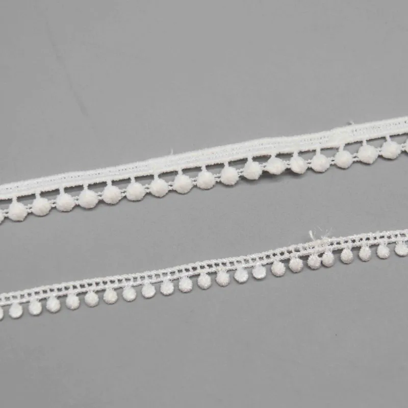 Two sizes of white pompom edging laid parallel on a gray background.