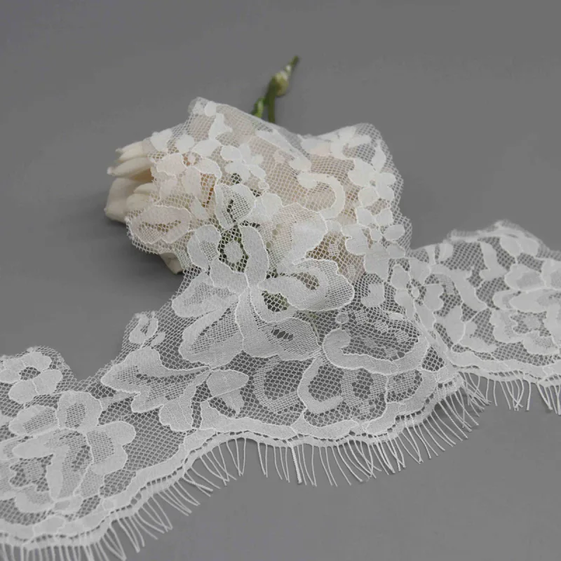 White floral lace draped over a white rose, showing its mesh ground and long fine fringe.