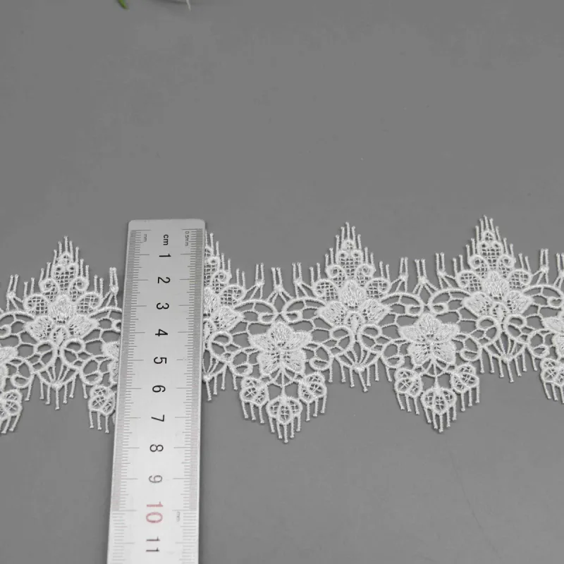 Ein senkrechtes Lineal über der weißen Spitze mit spitzen Blumenmotiven und feinen Fransen.