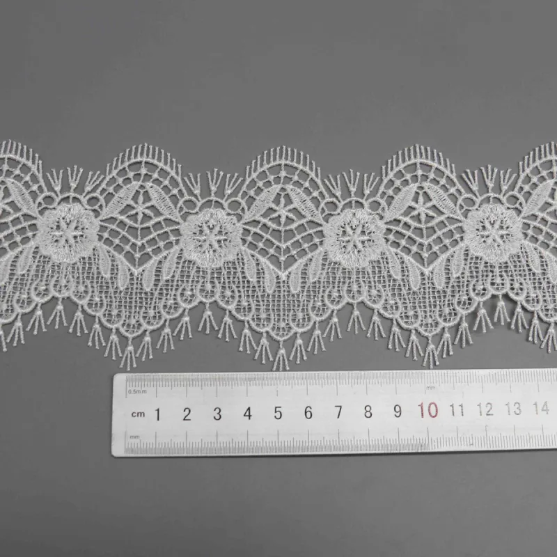 Ein waagerechtes Lineal unter weißer Spitze mit spitzen Blattformen zwischen runden Blumenmotiven.