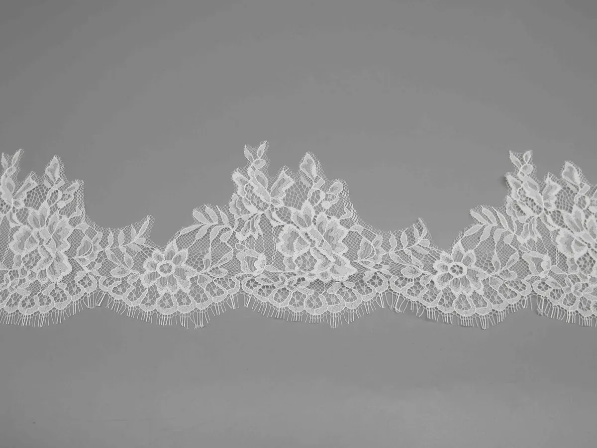 A length of white floral lace showing repeated leafy peaks and connected flower motifs.