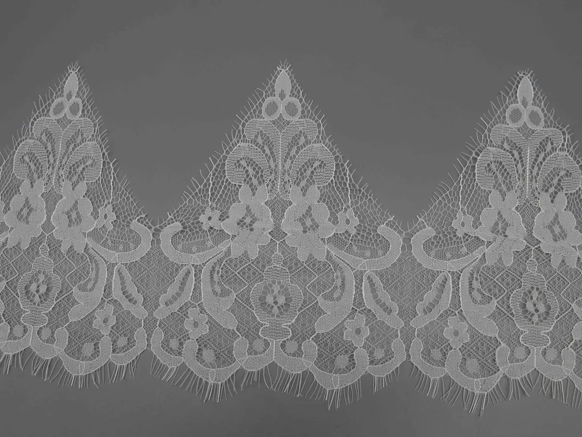 A wide view of three repeating pointed motifs across the white lace border.