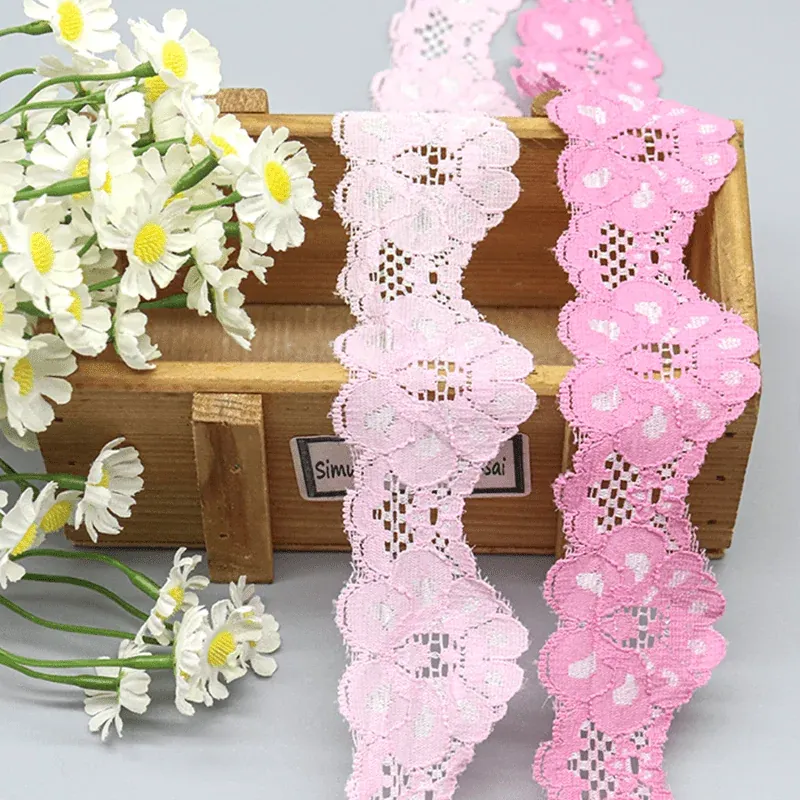 Zwei rosa florale Spitzenbänder, über einer hölzernen Präsentationsbox neben weißen Margeriten angeordnet