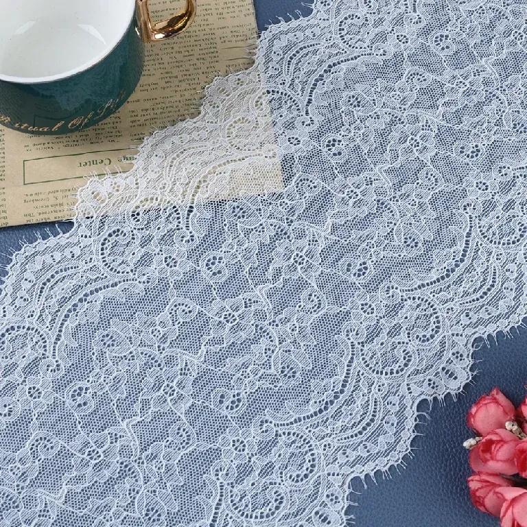 Galon de dentelle blanche à motifs floraux drapé près d’une tasse et de fleurs sur une surface sombre.