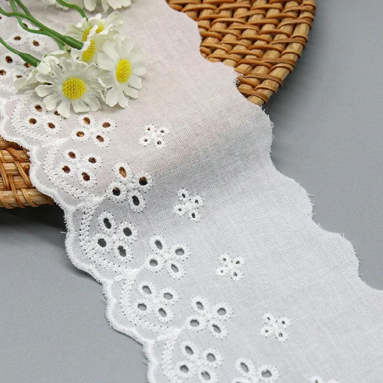 Galon de broderie anglaise blanc drapé près d’un panier tressé et de fleurs blanches.