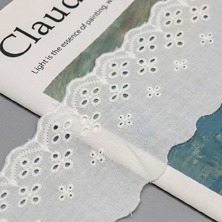 Galon de broderie anglaise blanc posé sur un livre d’art, laissant voir ses ajours floraux brodés.
