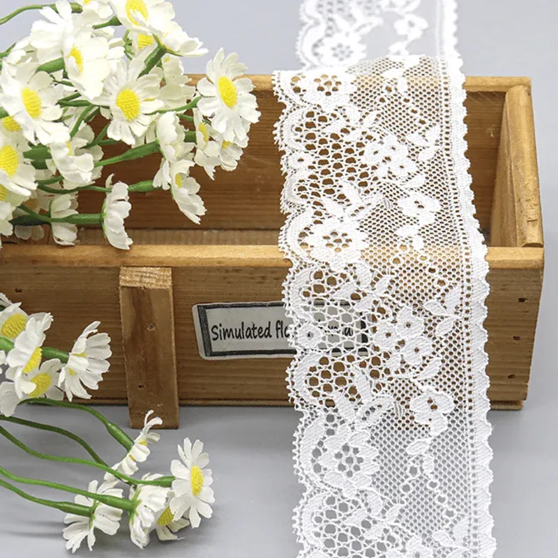 Galon de dentelle blanche à motifs floraux suspendu sur une boîte en bois près de marguerites.