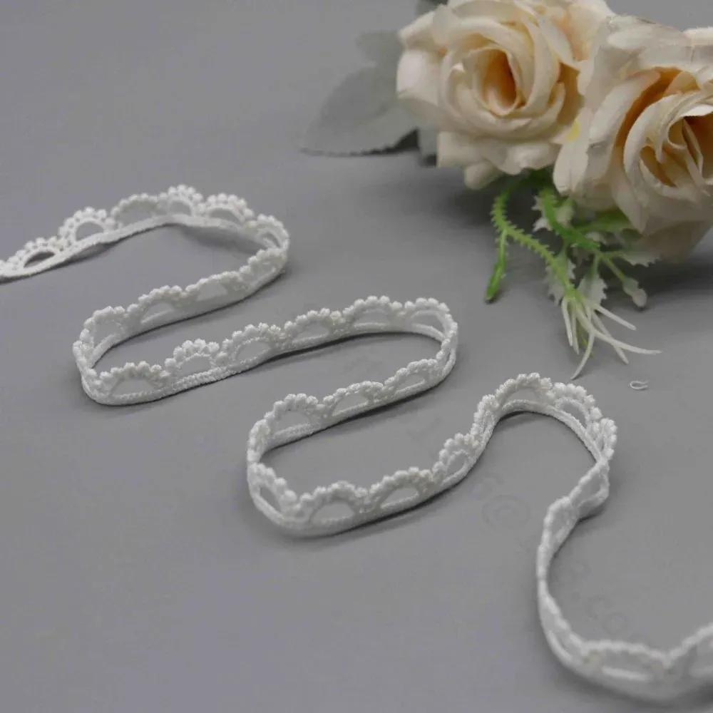 Galon de dentelle blanche à festons en éventail disposé en vagues lâches sous des roses crème.
