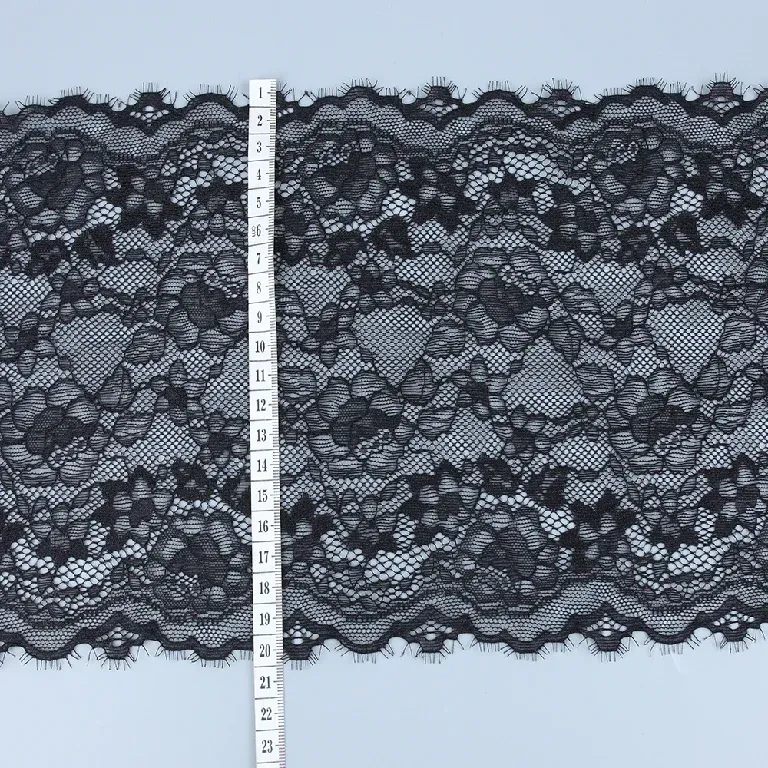Un mètre ruban placé en travers d’un galon de dentelle florale noire aux bords festonnés. Un mètre ruban placé en travers d’un galon de dentelle florale noire aux bords festonnés.