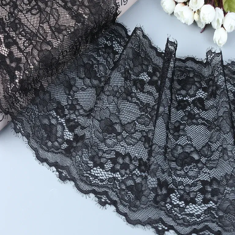 Galon de dentelle florale noire disposé en plis souples à côté de fleurs blanches.