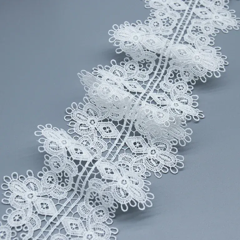 Tira de encaje floral blanco con relieve dispuesta en ondas sueltas sobre una superficie gris. Tira de encaje floral blanco con relieve dispuesta en ondas sueltas sobre una superficie gris.