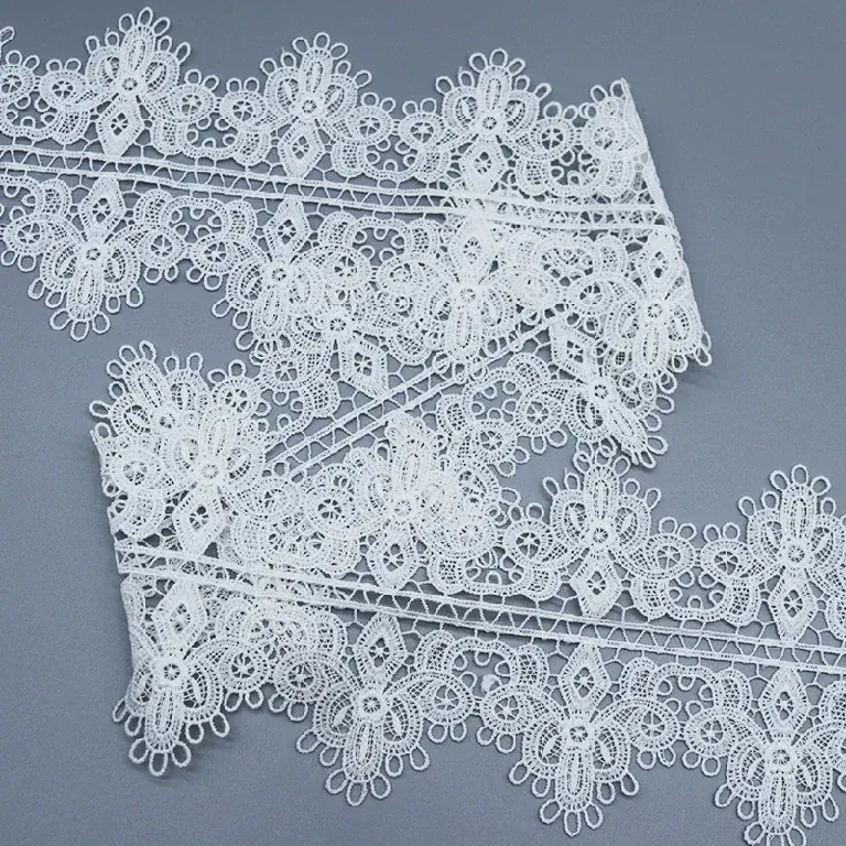 Tira de encaje floral blanco doblada sobre sí misma para mostrar el dibujo de bucles en relieve.