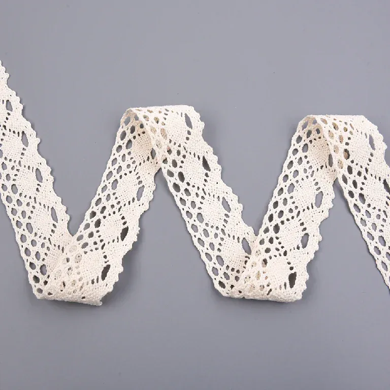 Galon de dentelle crème à motif d’ovales disposé en ondulations en zigzag sur une surface grise.