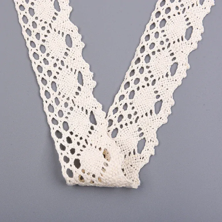 Galon de dentelle crème à motif d’ovales plié en V sur une surface grise.