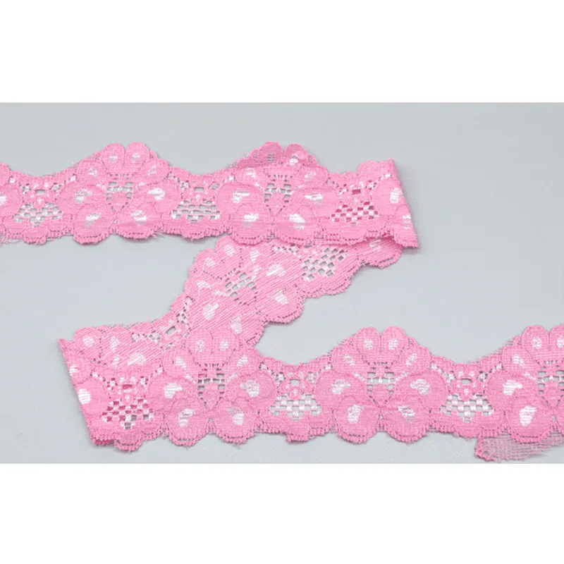 Galon de dentelle rose vif à motifs floraux disposé en courbes superposées sur une surface grise.