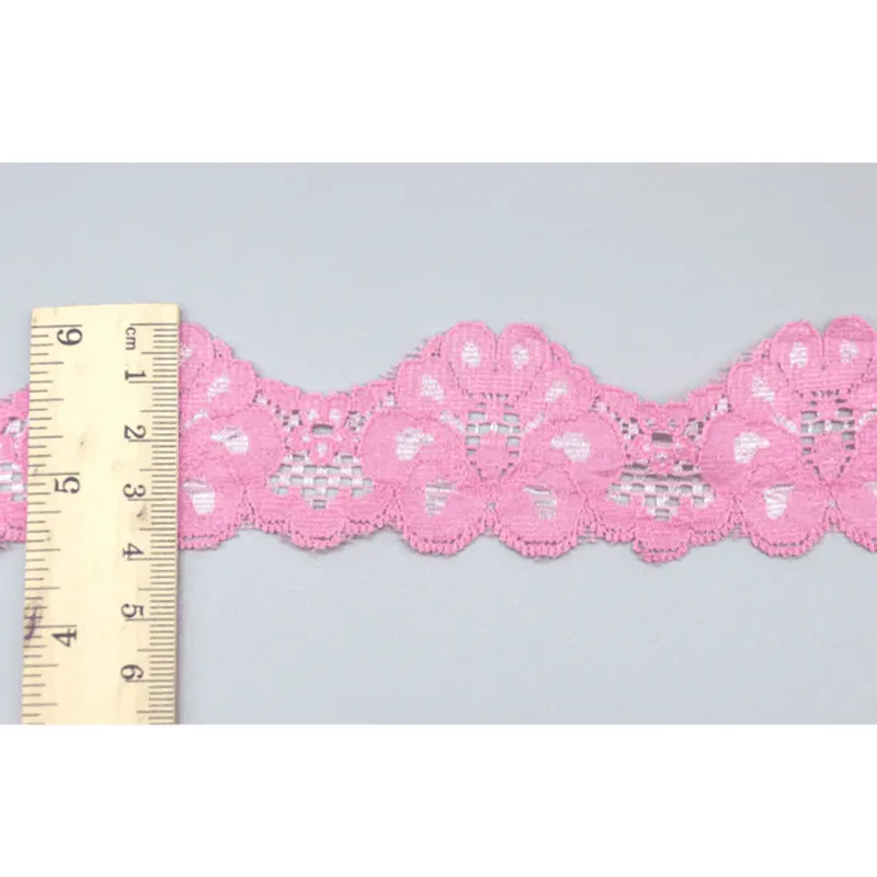 Un mètre ruban posé en travers d’un galon de dentelle rose vif à motifs floraux et bords festonnés.