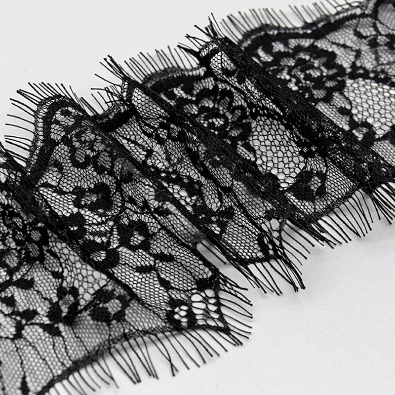 Galon de dentelle noire à motifs floraux posé en diagonale sur une surface grise, laissant voir ses bords finement frangés.