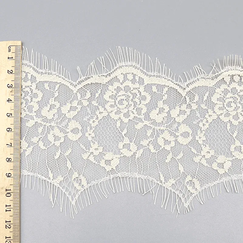 Un mètre ruban posé en travers d’un galon de dentelle ivoire à motifs floraux et bords finement frangés.