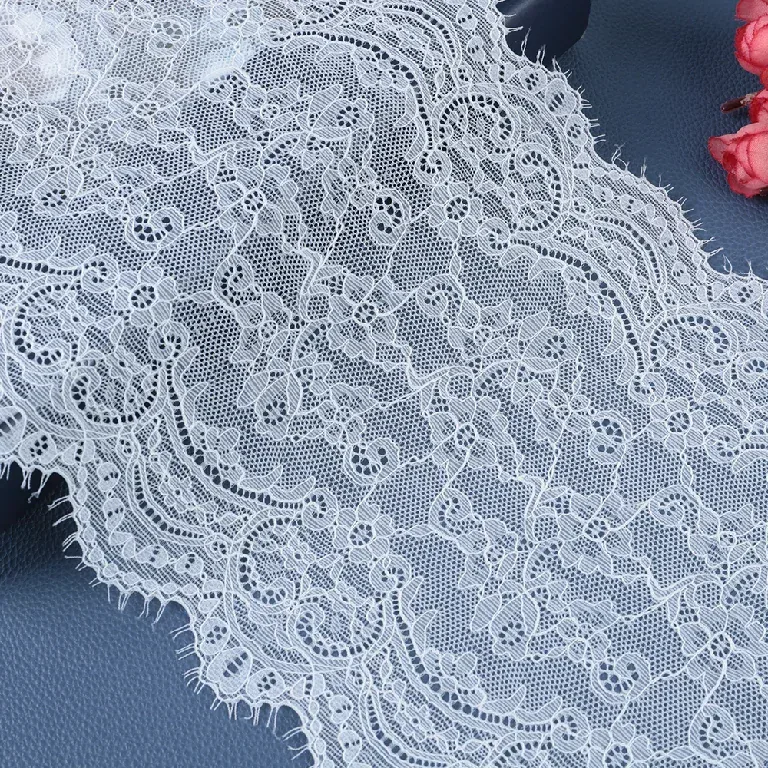 Galon de dentelle blanche à motifs floraux disposé en plis souples près de fleurs roses. Galon de dentelle blanche à motifs floraux disposé en plis souples près de fleurs roses.