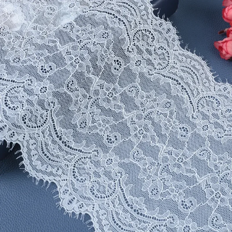 Galon de dentelle blanche à motifs floraux disposé en plis souples près de fleurs roses.