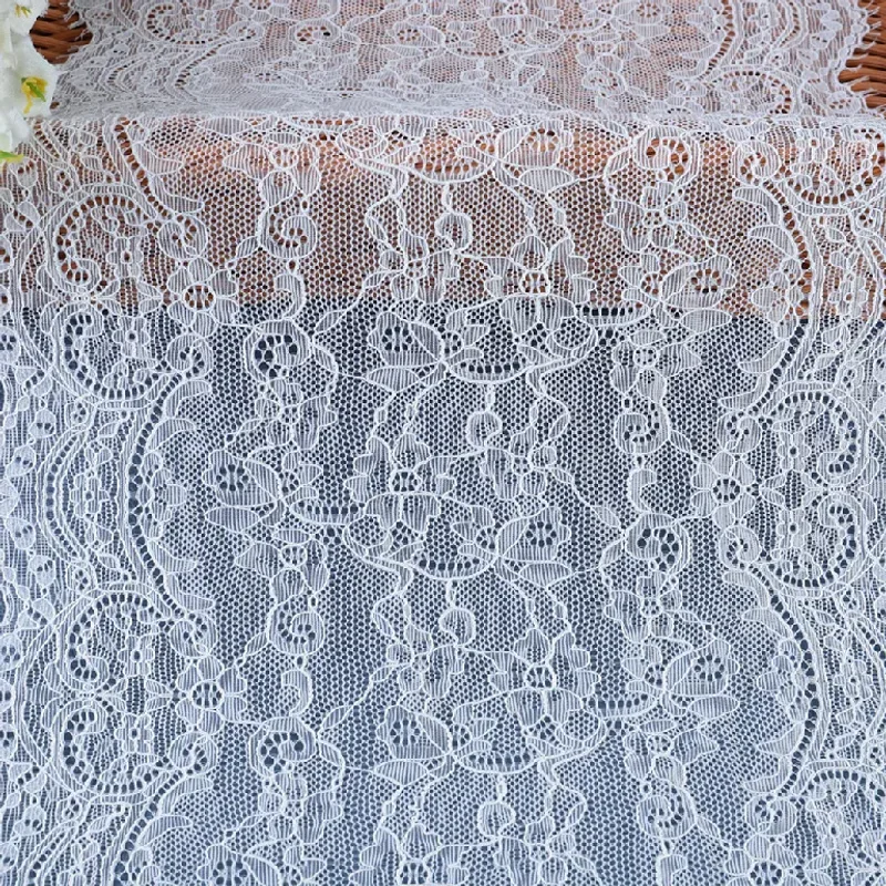 Gros plan sur un galon de dentelle blanche à motifs floraux, aux plis superposés et aux bords finement frangés.