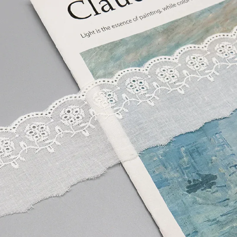 Galon de broderie anglaise blanc à motifs floraux posé en diagonale sur un livre d’art.