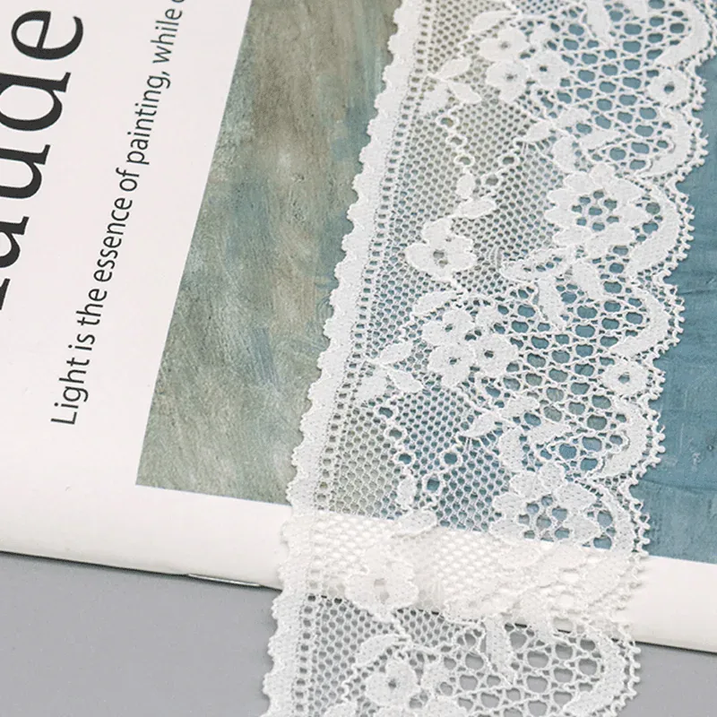 Galon de dentelle blanche à motifs floraux posé près d’une couverture de livre imprimée.