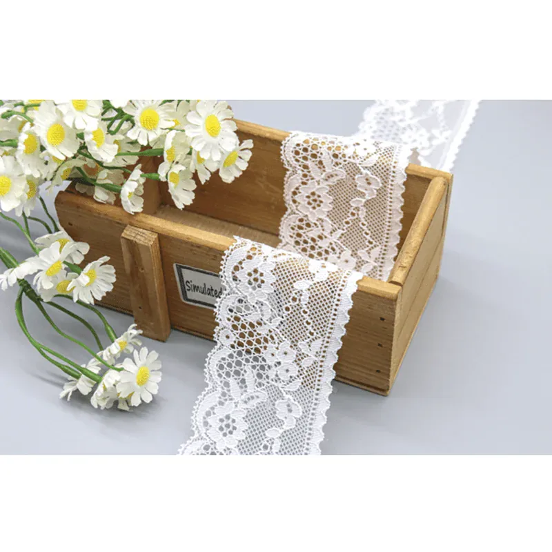 Galon de dentelle blanche à motifs floraux drapé sur une boîte en bois et des marguerites.