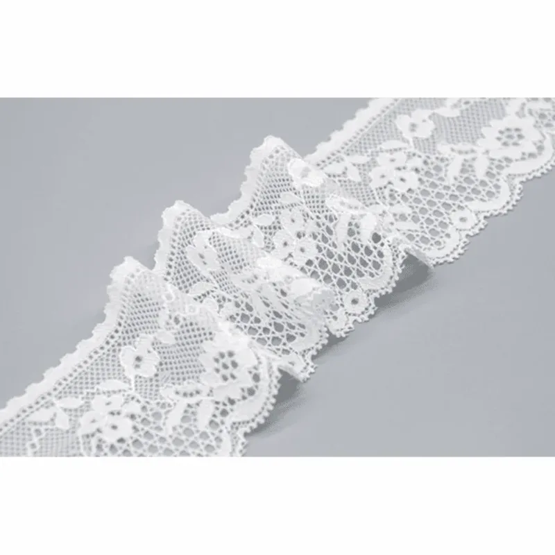Galon de dentelle blanche à motifs floraux disposé en vagues souples sur une surface grise.
