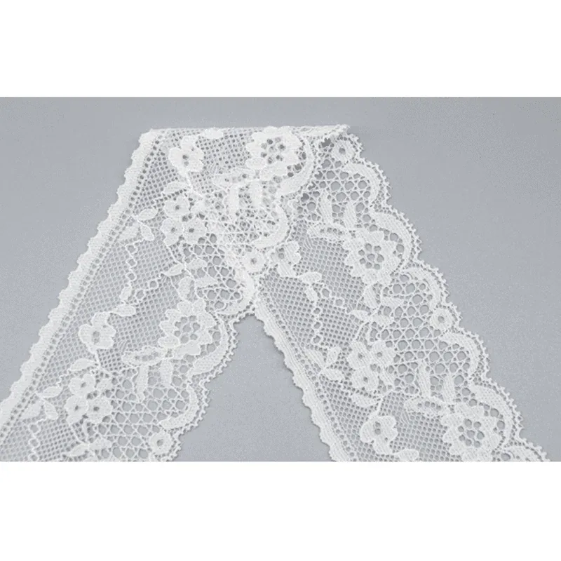 Galon de dentelle blanche à motifs floraux plié en V étroit sur une surface grise.