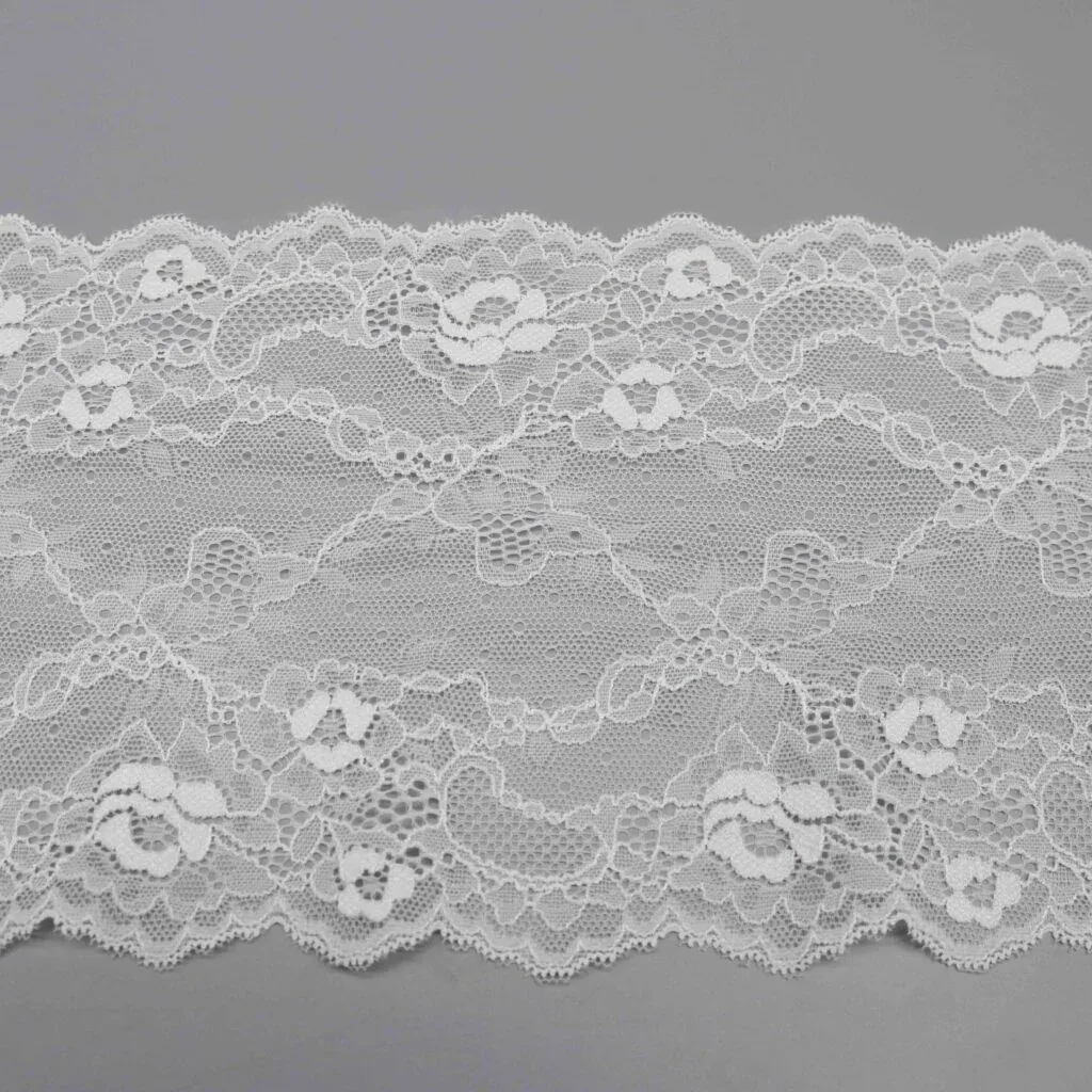 Une section à plat de large dentelle blanche à motifs de roses et bords festonnés. Une section à plat de large dentelle blanche à motifs de roses et bords festonnés.