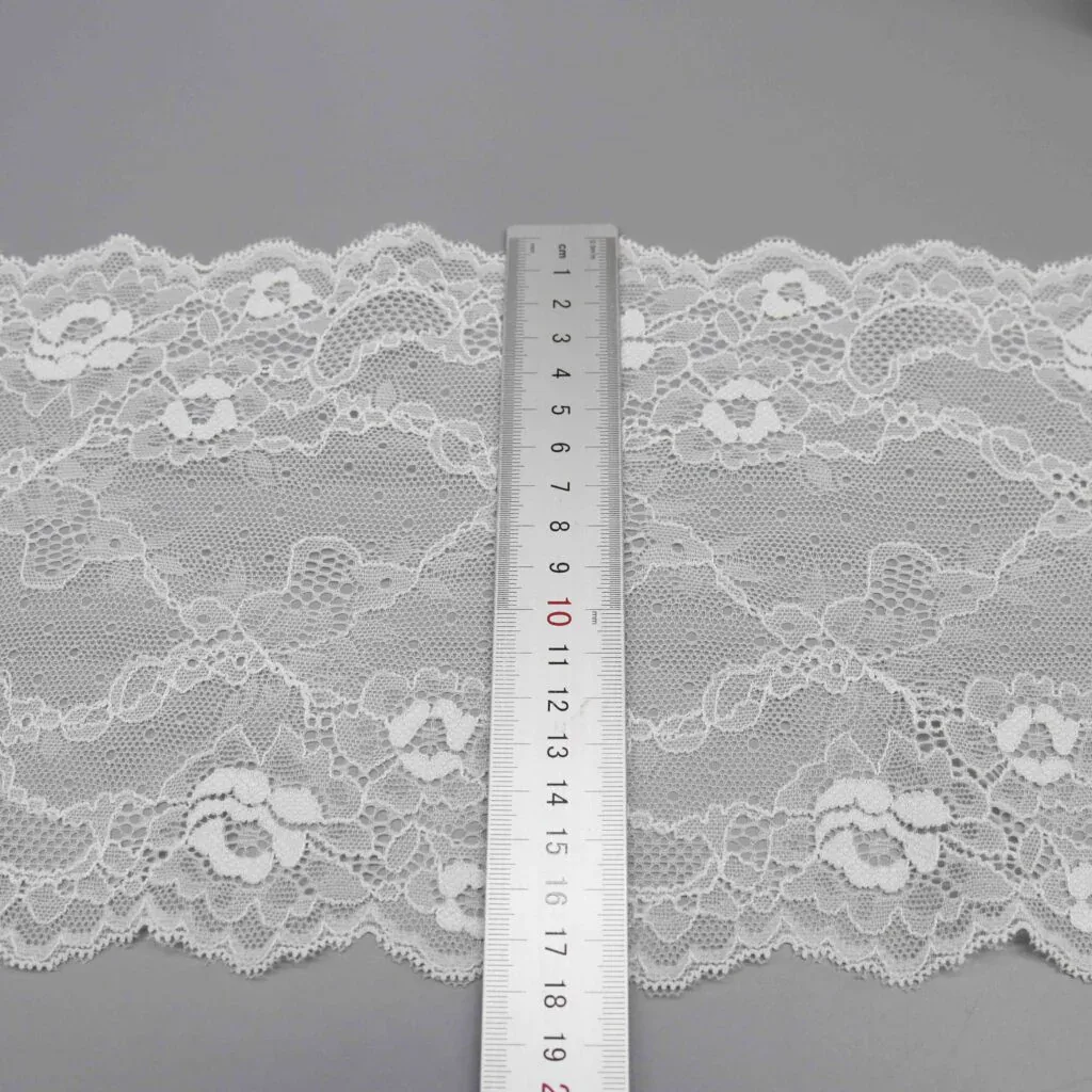 Une règle posée en travers d’une large dentelle blanche à motifs floraux, sur une surface grise. Une règle posée en travers d’une large dentelle blanche à motifs floraux, sur une surface grise.