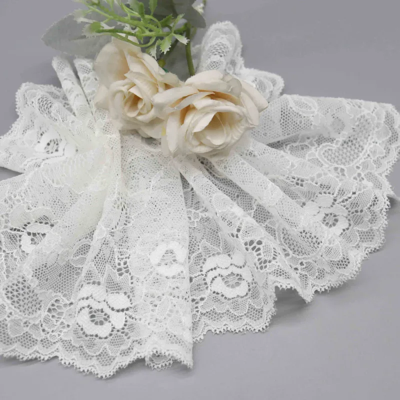 Large dentelle blanche à motifs floraux froncée en éventail sous des roses crème.