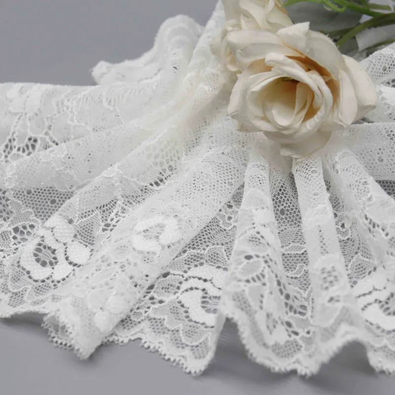 Large dentelle blanche à motifs floraux disposée en plis autour de roses crème.