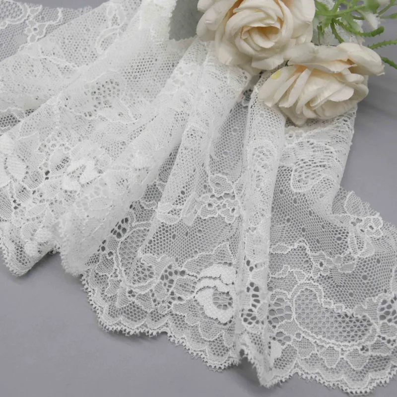 Gros plan sur une large dentelle blanche à motifs floraux et bords festonnés sous des roses crème.